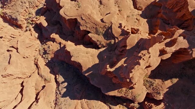 Directly above aerial view captures vast red rock formations in Kyrgyzstan at sunrise. Rugged landscape showcases geological beauty under bright daylight.