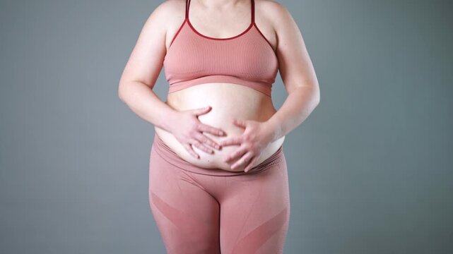 Fat woman in corrective tights, flabby belly after pregnancy, overweight female body on gray studio background