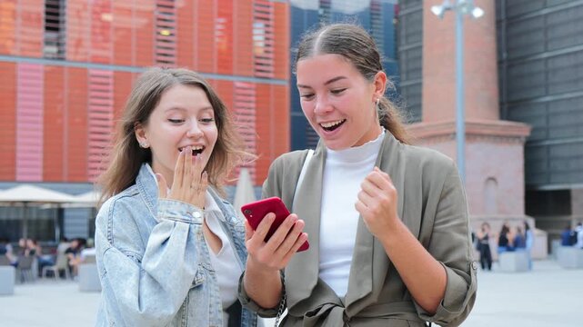 Joyful friends share an exhilarating moment as they discover something exciting on their smartphone, showcasing their happiness and strong bond through laughter and excitement in their interaction.
