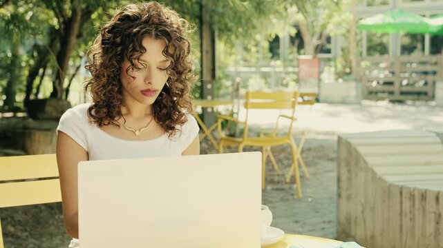 Independent young adult woman working from a stylish outdoor cafe using her smartphone. Summer urban setting representing freedom, autonomy and flexible lifestyle.