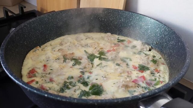 Cooking amlet with herbs in a frying pan close-up