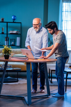 Two Indian generations reviewing income reports and submitting taxes online at home using laptop