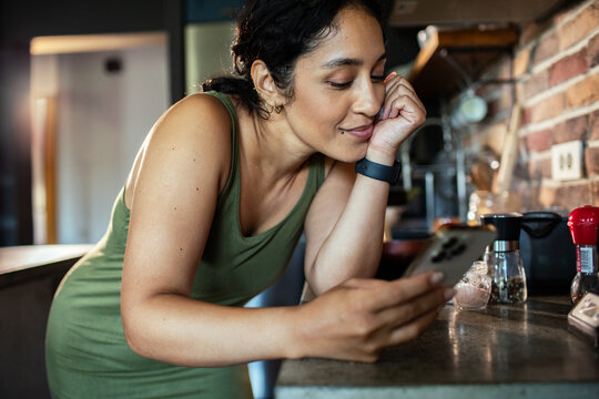 Young woman using smartphone at home kitchen counter