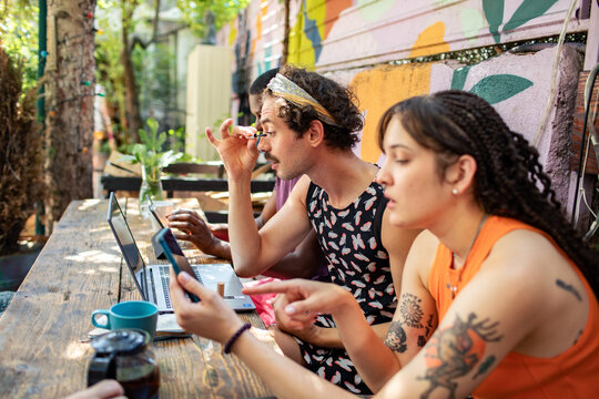 Friends coworking at outdoor cafe while applying makeup