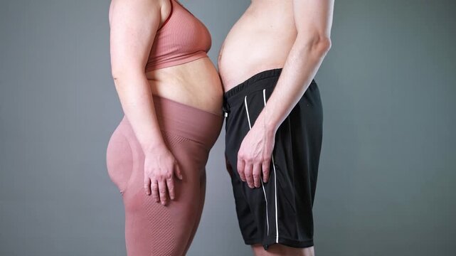 Fat couple doing vacuum exercise, man and woman inhale and exhale their stomachs during a breathing exercise, bellies in yin yang shape, breathwork and fitness, gray background