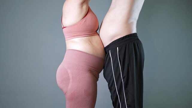 Fat couple doing vacuum exercise, man and woman inhale and exhale their stomachs during a breathing exercise, bellies in yin yang shape, breathwork and fitness, gray background