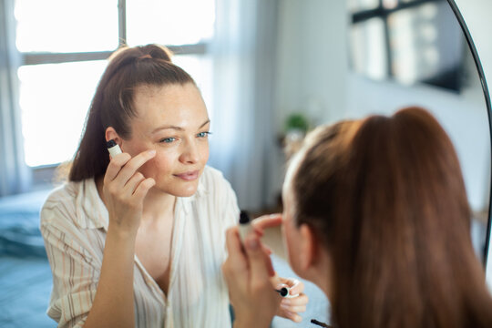 Woman applying concealer at home mirror