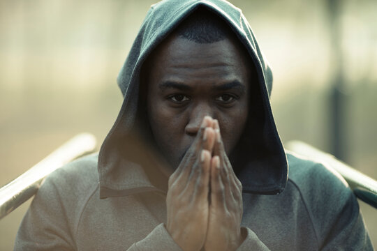 Focused man in hoodie with praying hands outdoors