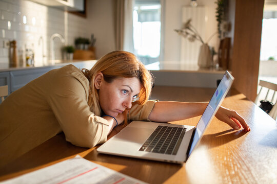 Tired woman working on laptop at home kitchen table