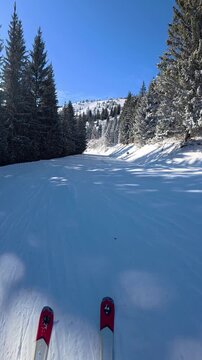 Beautiful POV ski landscape on the mountains. Skier skis down a snowy mountain trail in sunny weather.