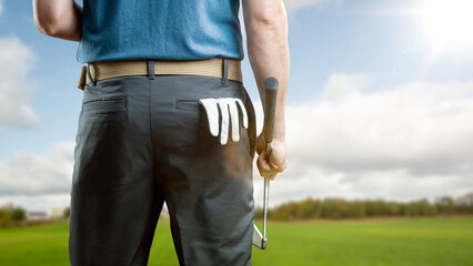 Rear view of a golfer holding an iron with a golf glove in the back pocket