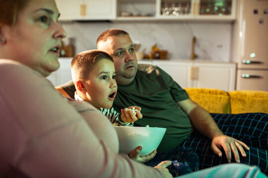Family watching tv with popcorn on the sofa at home