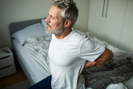 Mature man with back pain sitting on bed at home