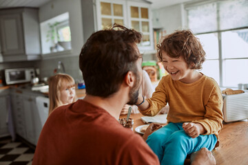 Obraz premium Smiling child feeding dad with spoon in family kitchen