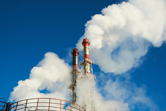 Two chimneys of a natural gas heating plant partially hidden by dense white steam. Water vapor and condensation cloud against a blue sky, winter utility background.
