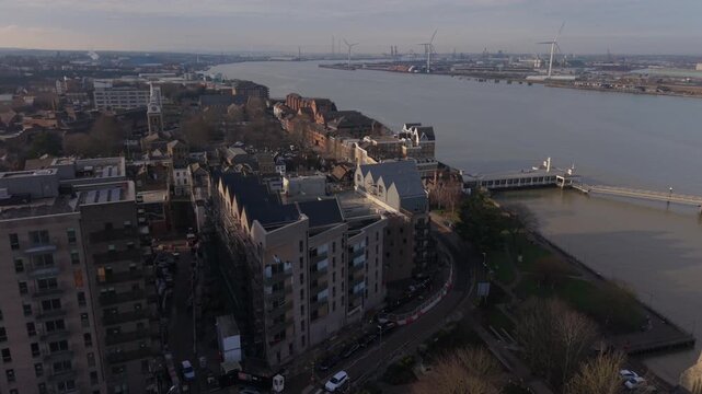 Aerial view of Gravesend town center with apartment buildings. Flying towards historic Gravesend Pier and river Thames. Tilbury Docks with tall spinning wind turbines in the background.
