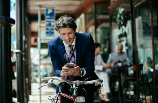 Businessman using smartphone beside bicycle outside city cafe
