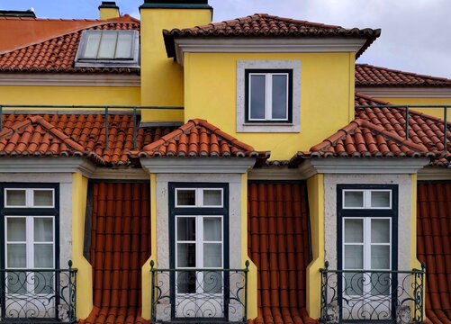 Photo of a charming example of traditional Lisbon architecture, featuring a warm yellow facade and classic terracotta mansard roof tiles. 