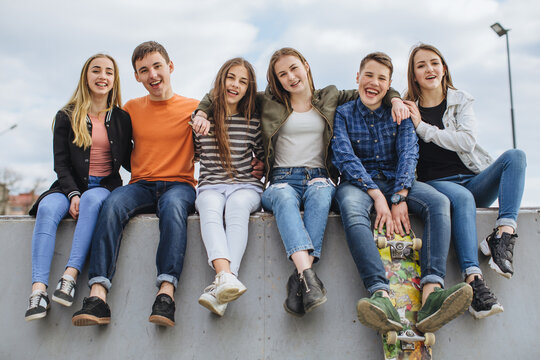 Group of diverse teenagers sitting together at skatepark, smiling at camera, embracing friendship and youth culture