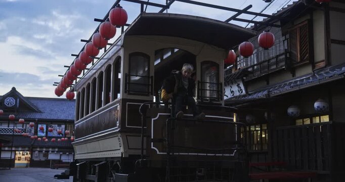 Young boy playing on silhouetted Japanese tram at dusk