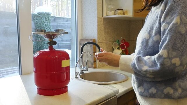 A young Ukrainian woman lights a gas stove with a match to make herself coffee during a power outage. The intimate kitchen scene highlights everyday resilience and adaptation to electricity shortages 