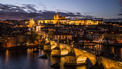 Evening view of Prague Castle and Charles Bridge. The buildings shine brightly against the night sky, reflecting in the Vltava River. The scene captures the beauty of the city.