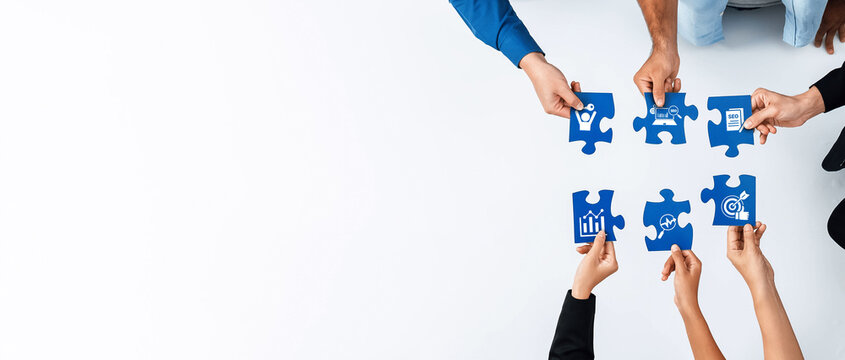 Overhead view of diverse hands assembling blue puzzle pieces symbolizing business concepts such as growth, collaboration, and strategy in a creative workspace. Amity