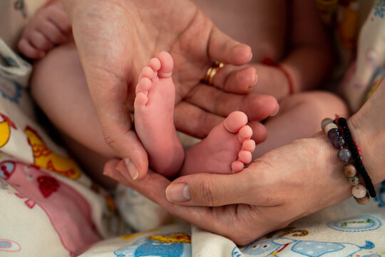 Close-up of a newborn baby&rsquo;s feet held in adult hands. A parent gently touches the tiny toes, showing tenderness, care and family bonding during early childhood.