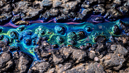 Macro shot of iridescent oil slick shimmering on wet asphalt or rock surface