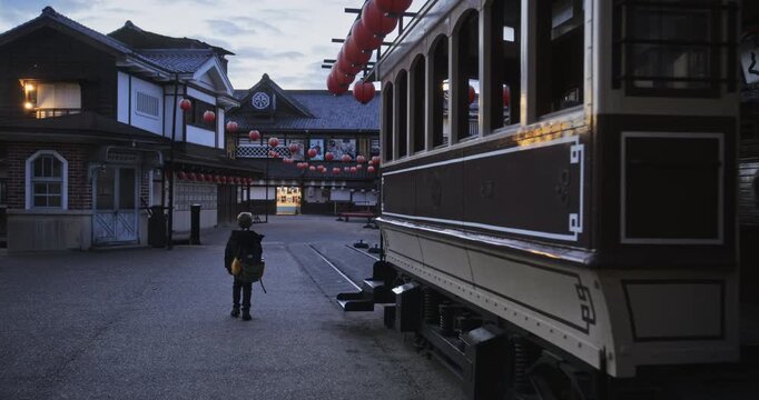 Little blond boy walking through old Japanese town near trolly - wide shot