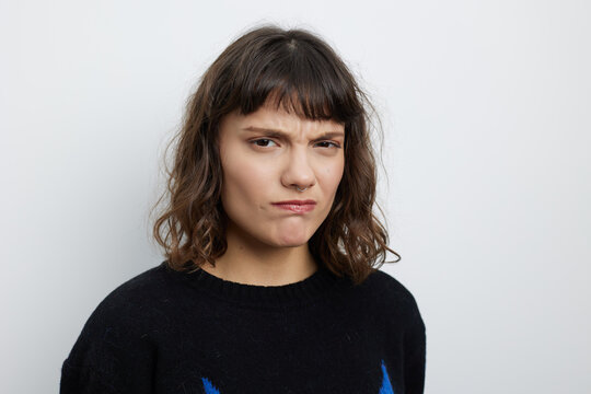 Portrait of a young woman with a puzzled expression, wearing a dark sweater against a neutral studio backdrop. The raised eyebrow and unsure look convey confusion and a candid mood.