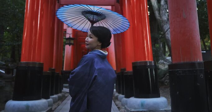 Japanese woman wearing kimono and holding umbrella in front of tori gates