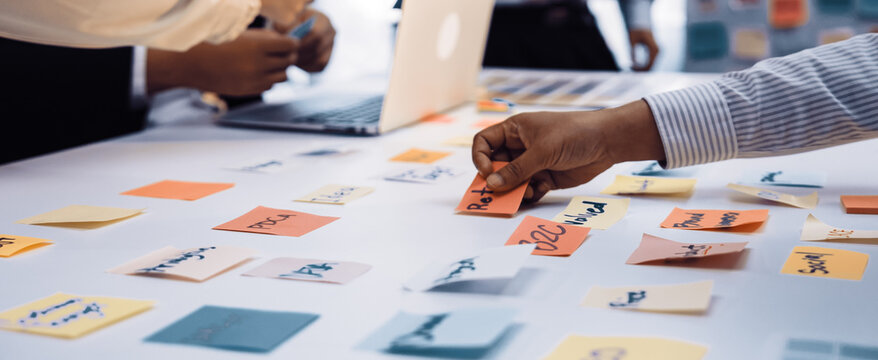 A dynamic office scene showcasing a team engaged in collaborative brainstorming using colorful sticky notes on a table, with a laptop in the background. SACTR