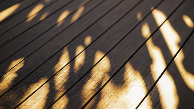 Warm golden hour sunlight falls across textured wooden deck planks, dappled green leaf shadows creating a calm, rustic outdoor patio backdrop with soft evening glow