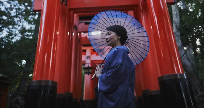 Slow motion of beautiful Japanese woman in kimono holding umbrella and standing under ancient tori gates