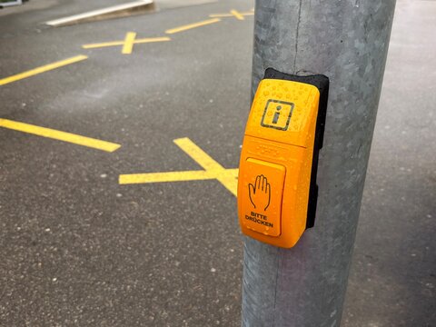 Close-up of yellow stop request button on metal pole at public transport stop.