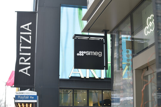 projecting sign outside Smeg, a home goods store, located at 2 Bloor W (and behind, Aritzia, a women's clothing shop at 50 Bloor St W (Holt Renfrew Centre), Toronto