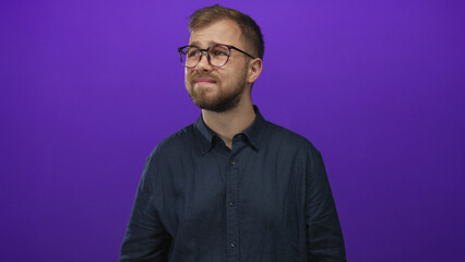 Fototapeta premium Man wearing glasses and a button shirt with visible face looking up toward a light in purple studio; confusion.