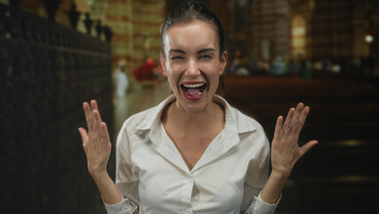 Woman with clenched fists and beaming smile stands in ornate church interior with wooden pews and stone columns  spiritual joy. © Krakenimages.com