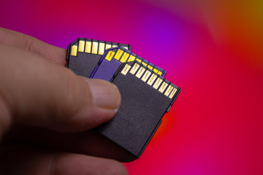 Holding multiple SD memory cards in a hand with a background of colorful light patterns