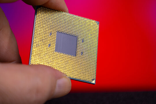 Close view of a hand holding a computer microprocessor with a shiny gold surface against a colorful background