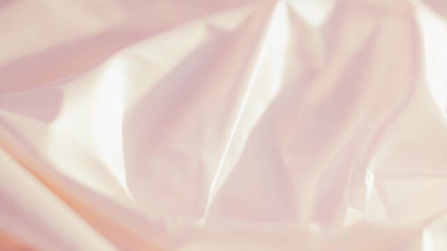 Crumpled light pink plastic with glossy creases and soft folds reflecting ambient light, creating an ethereal, translucent abstract background with gentle ripples and pastel glow