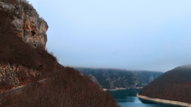 Flight along the wavy road passing on the mountain. Moving over the tops of dry trees and blue river. Montenegro.