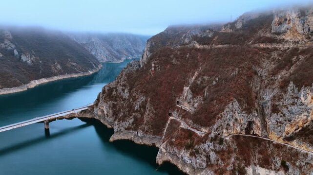 Cliff rocks crossed by the roads and tunnels. A bridge crosses the blue waterscape of the river among the mountains. Aerial view. Montenegro.