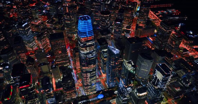 Footage over the blue neon top of the Salesforce Tower in midtown San Francisco, California, USA. Lively streets of metropolis at night from drone.