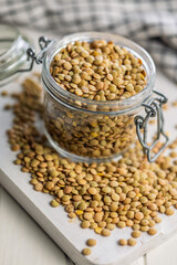 Uncooked green lentil in jar on white table.