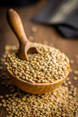 Uncooked green lentil in bowl on wooden table.