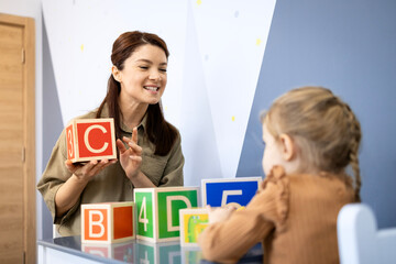 Speech therapist teaching child communication skills using alphabet blocks during an educational session, helping with speech and language development in a clinic © littlewolf1989