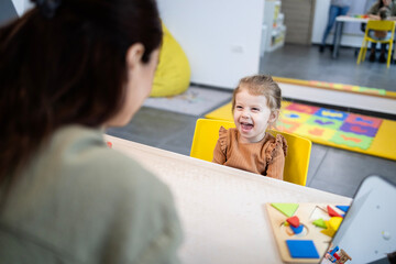 Speech therapist working with a happy little girl, helping her with early language development and...