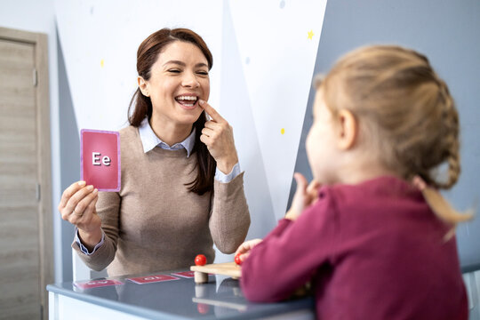 Speech therapist teaching child articulation and pronunciation using letter flashcard during a speech therapy session, focusing on speech development and language skills